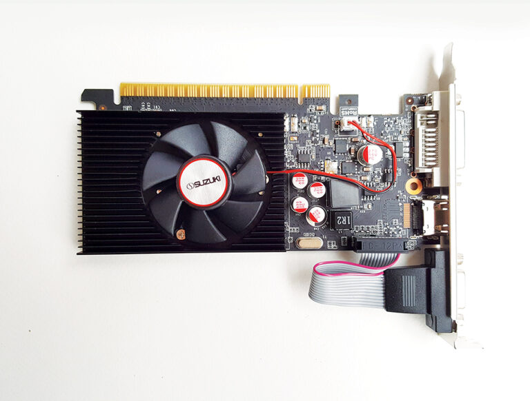 Top view of a Suzuki graphics card with a black cooling fan, heatsink, capacitors, and video output ports on a white backgrou