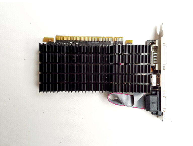 A low-profile graphics card featuring a large black passive heatsink, video ports, and a ribbon cable on a white background.