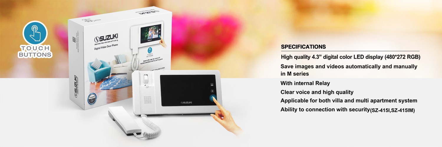 Hand touching the screen of a white Suzuki video door phone monitor next to its box and specifications.