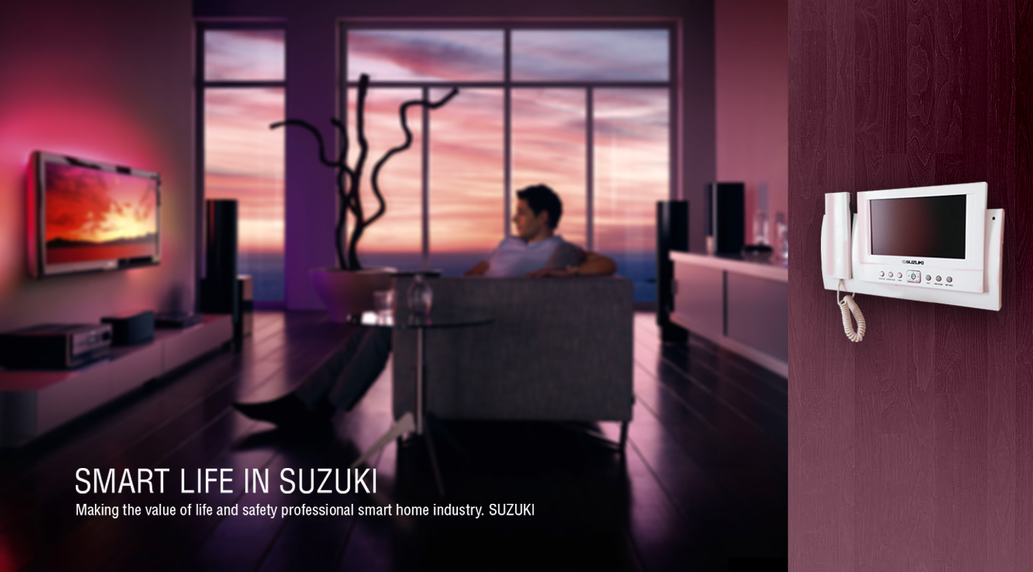 White Suzuki video intercom panel on a wall with a blurred modern living room background featuring a man relaxing near a wind