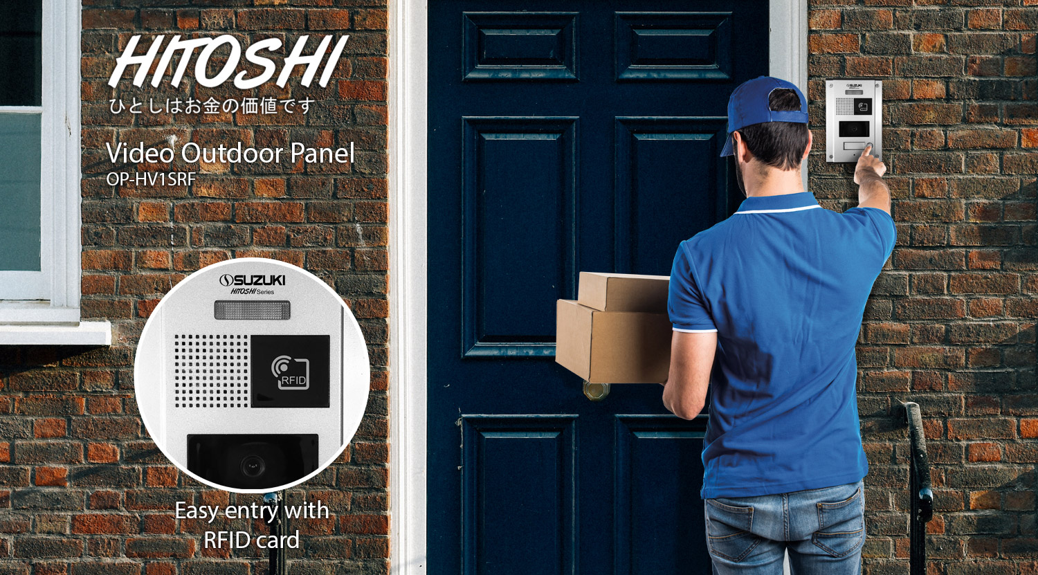 Delivery driver holding cardboard boxes presses the button on the silver Hitoshi video outdoor panel mounted on a brick wall.