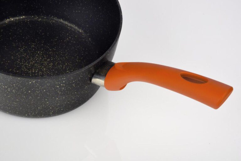 Close-up side view of a black granite-effect frying pan with a bright orange handle against a white background.